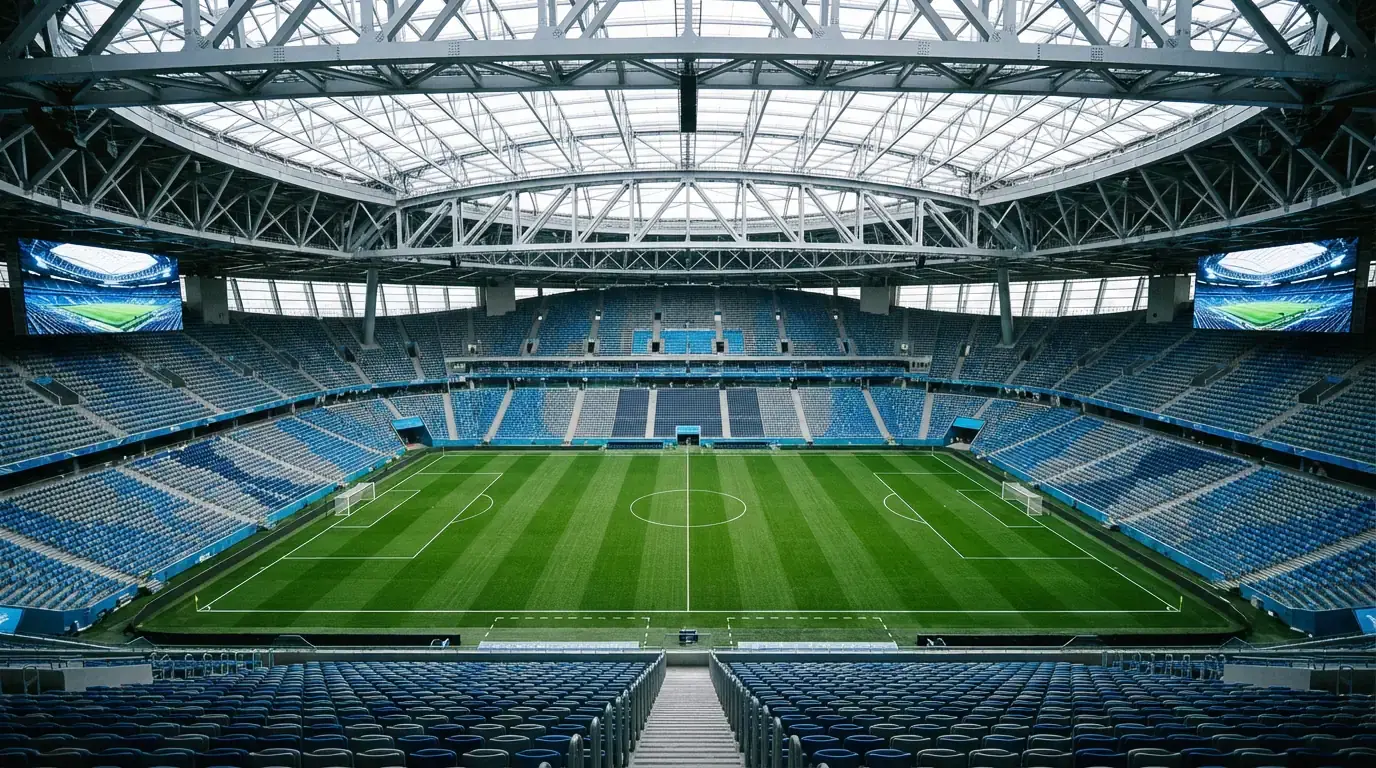 Innenansicht einer riesigen überdachten Fussballarena mit grünem Spielfeld, leeren Sitzreihen und beeindruckender Dachkonstruktion