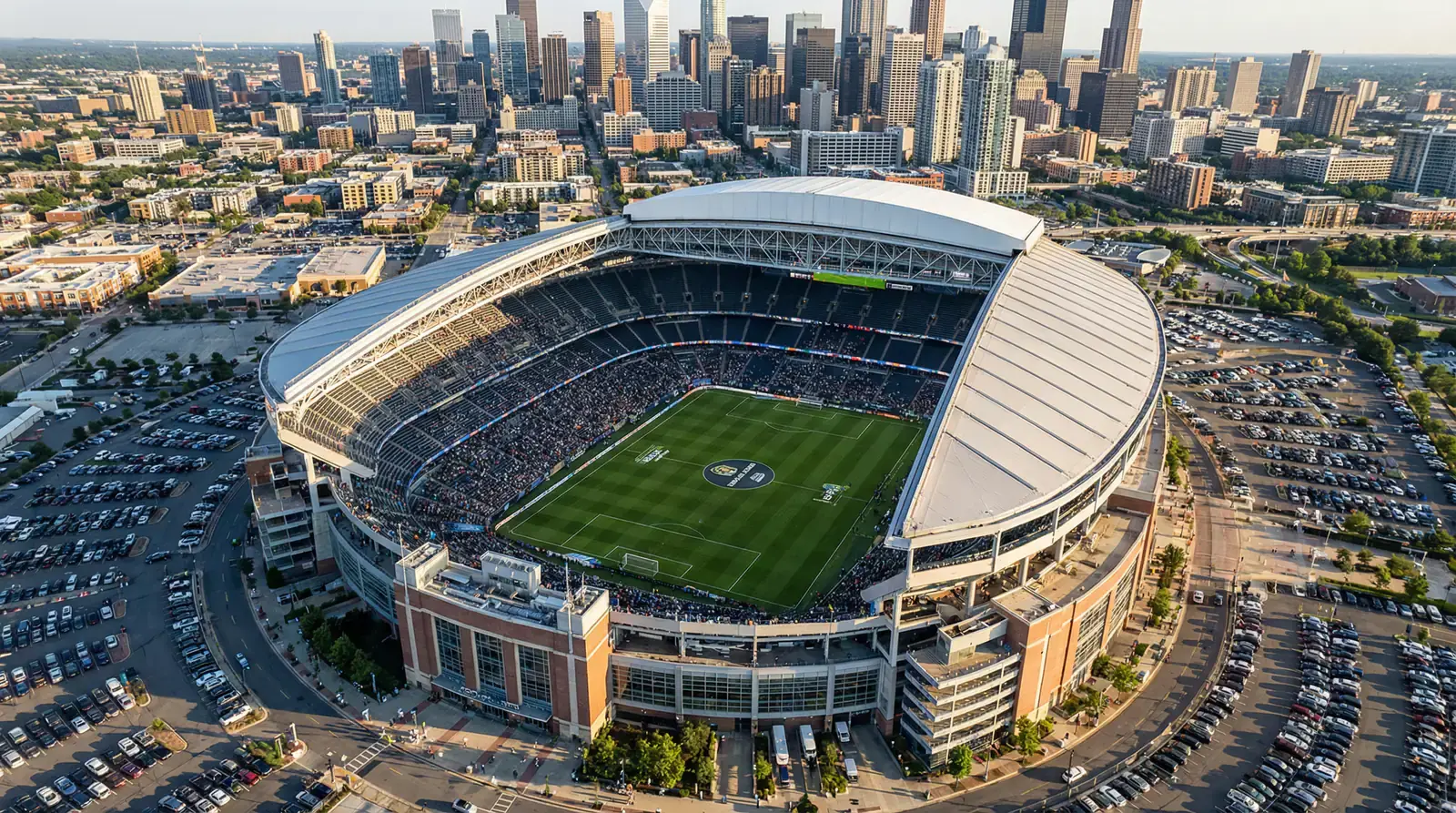 Luftaufnahme eines modernen Fussballstadions mit geöffnetem Dach bei Sonnenuntergang vor der Skyline einer nordamerikanischen Grossstadt